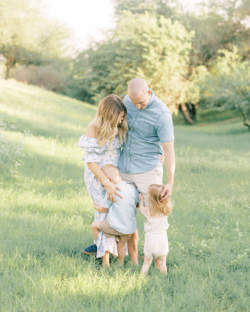 little boy and girl hugging mom and dads legs standing in the grass during full-service family photography session