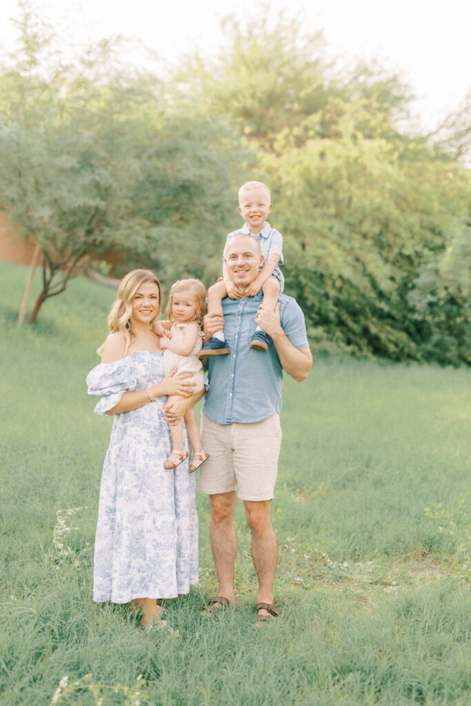 family photo of husband and wife holding their son and daughter standing in green grass.