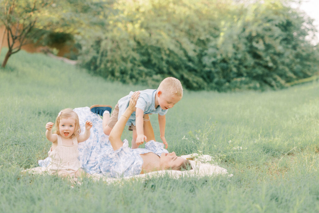 mom laying on grass playing with her son and her daughter