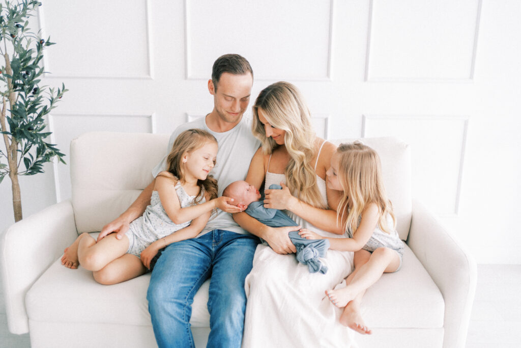 family sitting on couch while mom holds newborn baby brother in a sweet tender moment in Phoenix Arizona