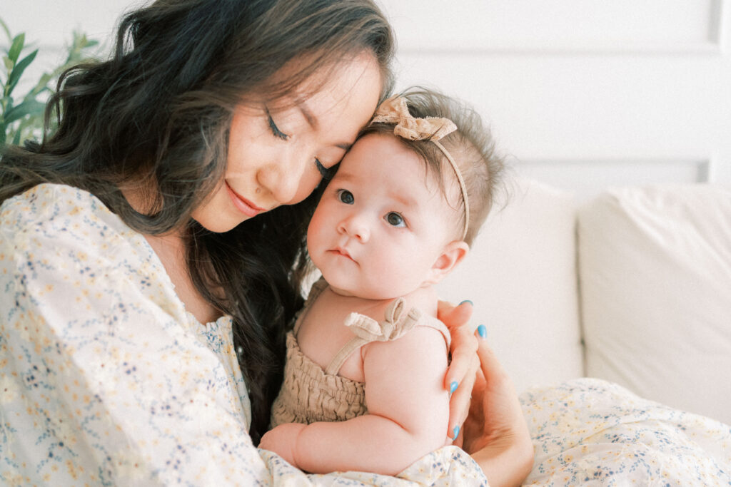 A close up photo of a mom in a light yellow floral dress snuggled up with her 7 month old daughter.