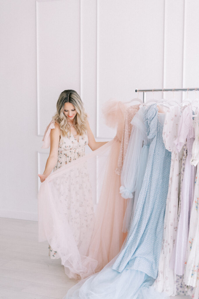 Nichole Pach holding a dress on a rack filled with beautiful maternity gowns in Phoenix.