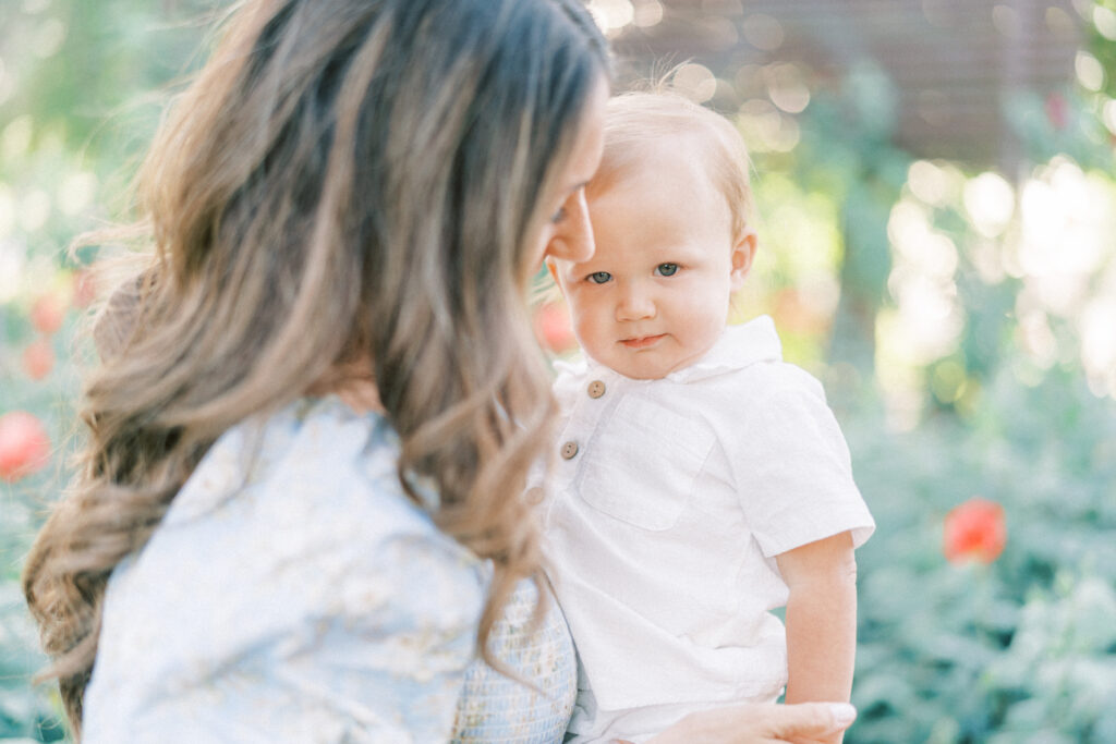 Close up image of mom and toddler with toddler looking at the camera in a rose garden in Mesa Arizona.