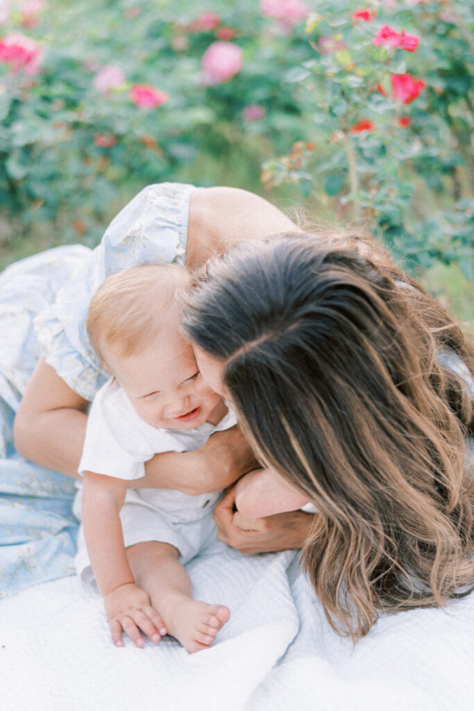 Mom in blue dress snuggled on the ground kissing her little toddler boy around roses in Phoenix Arizona.