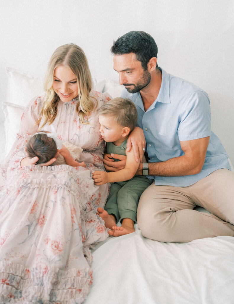 A mom in a pink dress in scottsdale Arizona sitting next to her toddler son and husband holding her new baby girl.