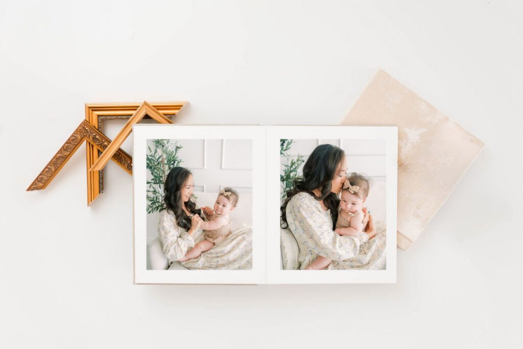 An open heirloom album showing a mom and 6 month old little girl sitting on a couch snuggling in Scottsdale Arizona. Gold frames also in photo.