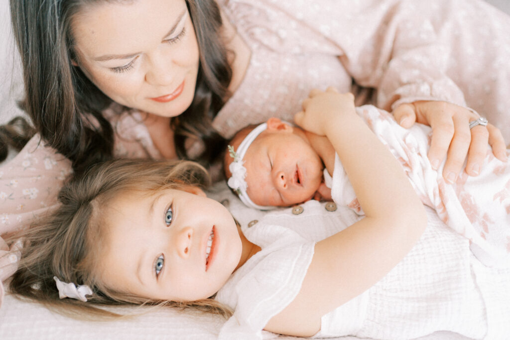 Mom, toddler daughter and newborn baby laying on the bed together in Mesa Arizona studio.