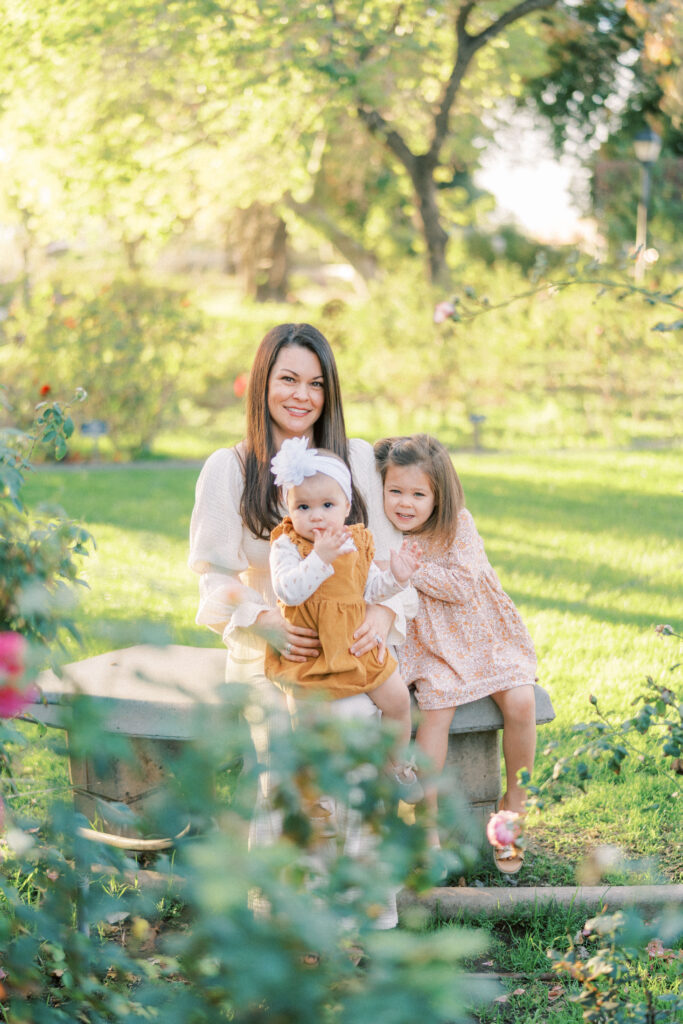 mom and two daughters sitting on a bench at a rose garden in Tempe Arizona.