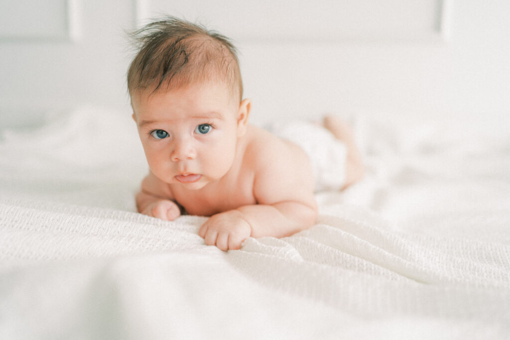 a 6 month old baby boy doing tummy time on white blanket during milestone session.